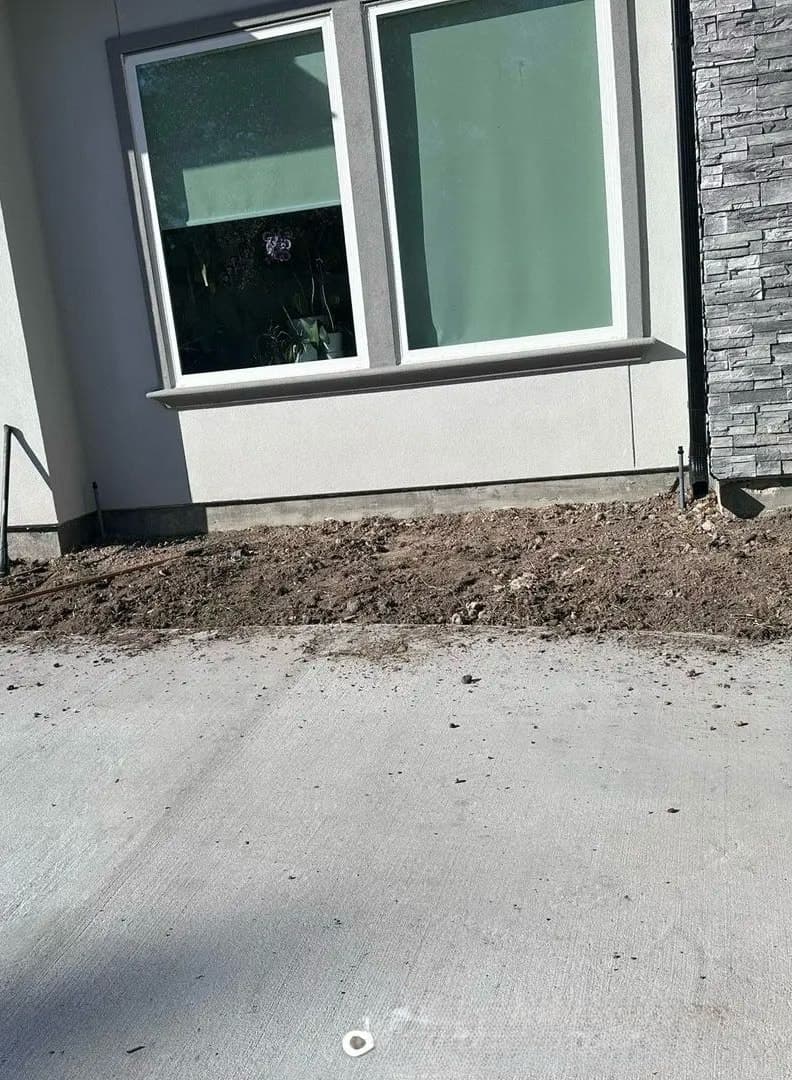 Bare, uneven soil in front of a house wall before the work