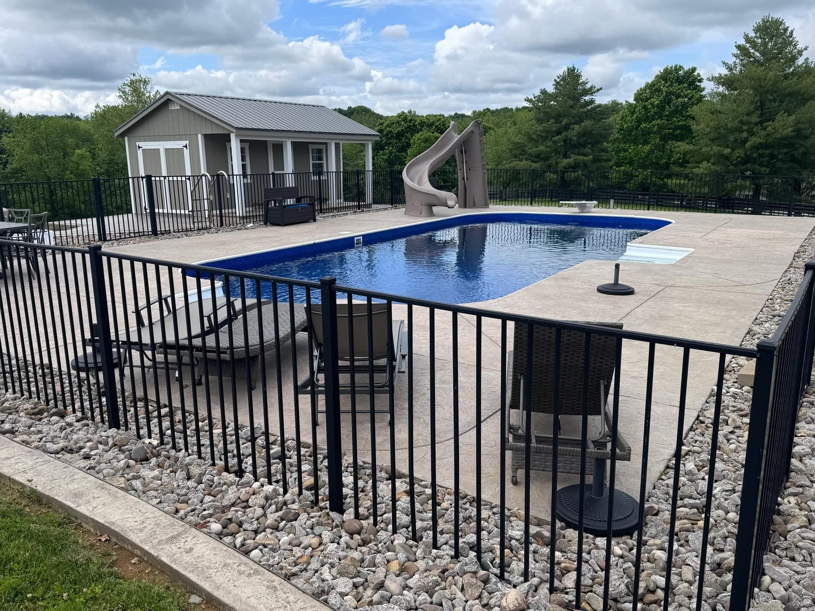 Pool area bordered with river rock and a black fence