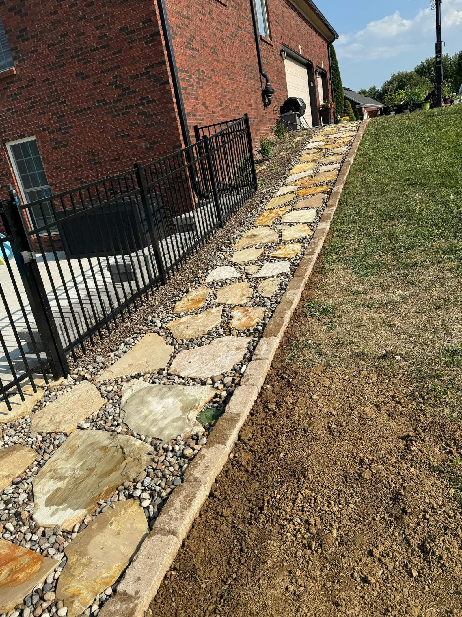 Flagstone path set in river rock with a paver border along a lawn